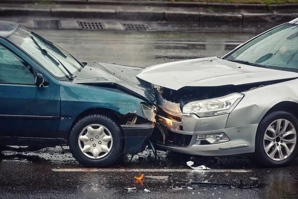 Two cars crashed head-on into each other on wet asphalt road.